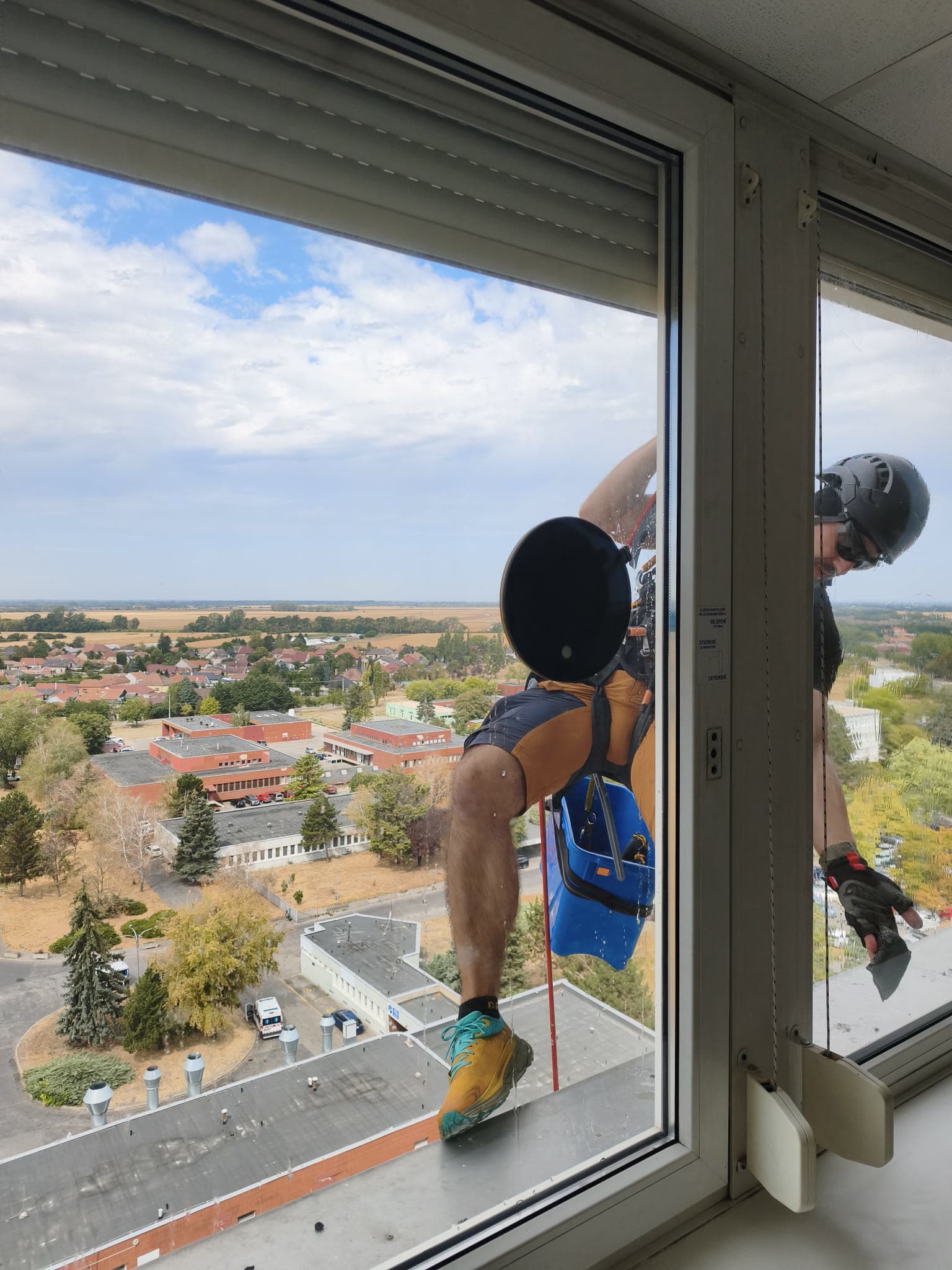 Výškový pracovník na lane umýva okno vo výške